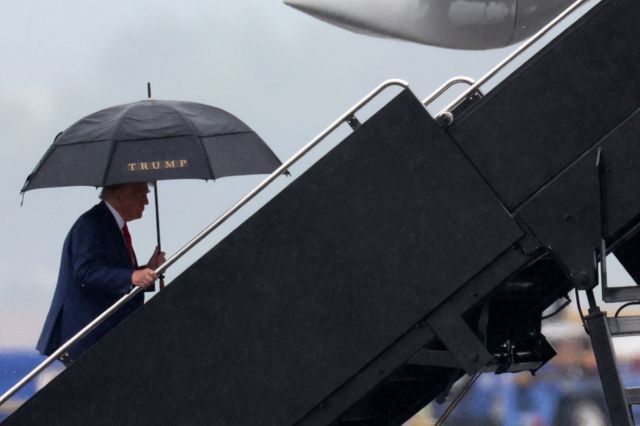Donald Trump sube a un avión con un paraguas