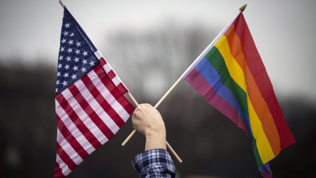 Manifestante segura bandeira americana e do arco-íris (março de 2017)