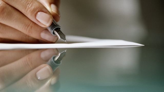 Una mano sostiene una pluma sobre un papel