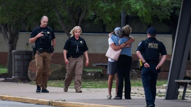 Policías se acercan a dos personas que se abrazan en una calle de Tulsa, Oklahoma, esperando noticias del tiroteo.