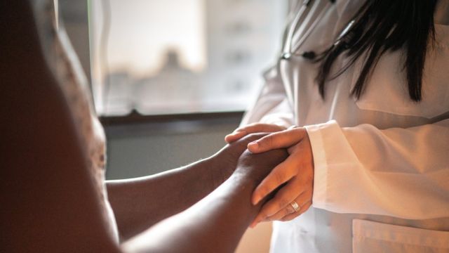 Mãos de médica juntas às de paciente