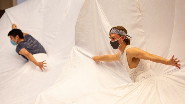 Dois homens de máscaras em tutus gigantes dançam em um palco