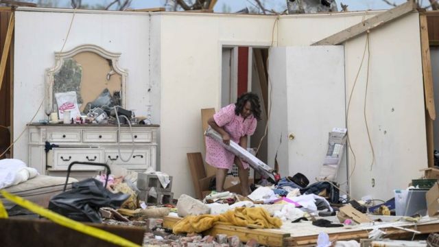 Una mujer recoge escombros en medio de una casa destruida.