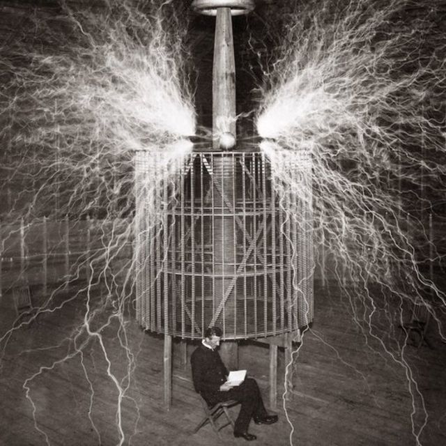 تيسلا جالسا في مختبره في كولورادو سبرينغز مع "جهاز الإرسال المُكبر" في عام 1899