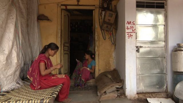 Duas mulheres sentadas em uma casa, vestidas com traje típico indiano