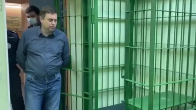 Norilsk Nickel power plant's director, Vyacheslav Starostin walking towards a cage in police custody