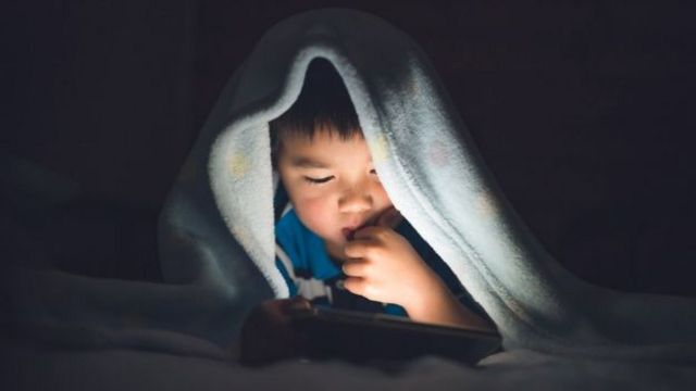 Dete drži mobilni telefon u krevetu