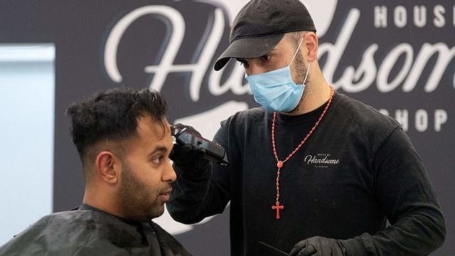Un coiffeur portant un masque facial coupe les cheveux d'un client à Wellington, en Nouvelle-Zélande