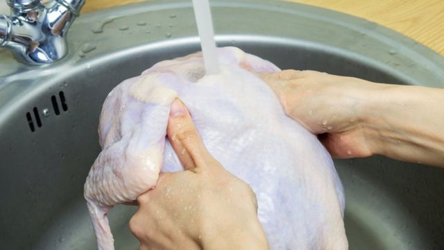 Pessoa lavando frango na pia