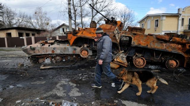 A man walks with his dog past a destroyed Russian tank in Ukraine.