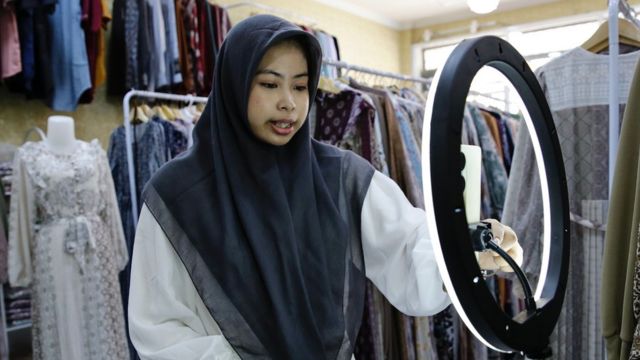 A woman uses a mobile phone to live-stream on an e-commerce platform at a shop in Depok, Indonesia.