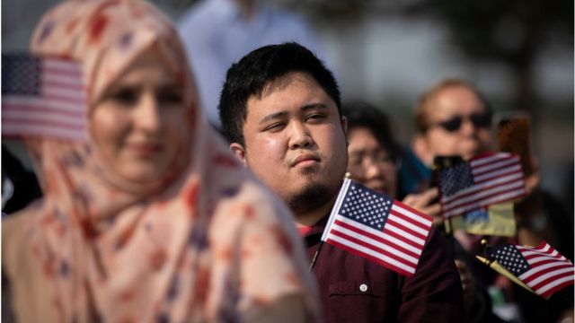 New American citizens wave American flags while 'America The Beautiful' is sung during a naturalisation ceremony