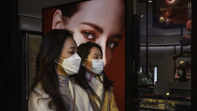 Chinese women wear protective masks as they walk by a luxury store while shopping in Sanlitun on March 10, 2020 in Beijing, China.