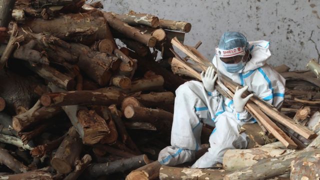 Un familiar sostiene trozos de madera en una pira en India.