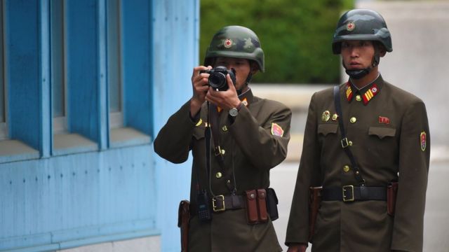 A North Korean soldier takes a photo as two soldiers look at the South side while US Vice President Mike Pence visits the truce village of Panmunjom in the Demilitarized Zone (DMZ) on the border between North and South Korea on 17 April 2017