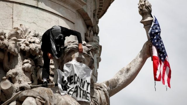 A banner and a US flag are placed on the Monument a la Republique during a protest against police brutality and the death in Minneapolis police custody of George Floyd