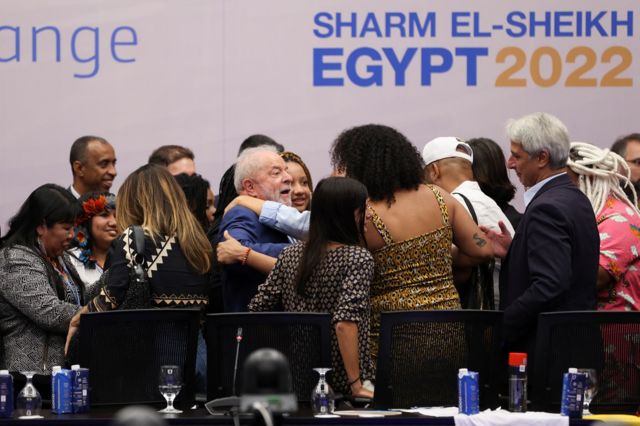 Lula abraçado por várias pessoas em evento