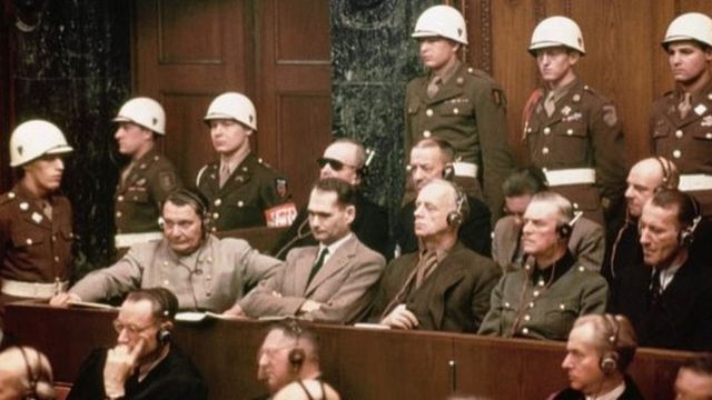 Um grupo de réus nazistas no tribunal, cercado pela polícia
