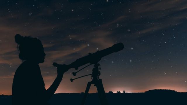 A woman looking at the night sky with a telescope