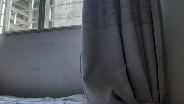 Fotografia mostra detalhe de cama com cortina e janela