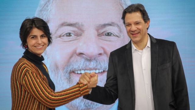 Manuela D'Ávila (esq.) e Fernando Haddad (dir.) em 'debate paralelo' no dia 9 de agosto, em frente a foto de Lula