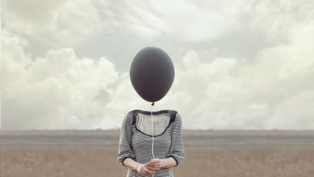 Una persona sosteniendo un globo en lugar de una cabeza.