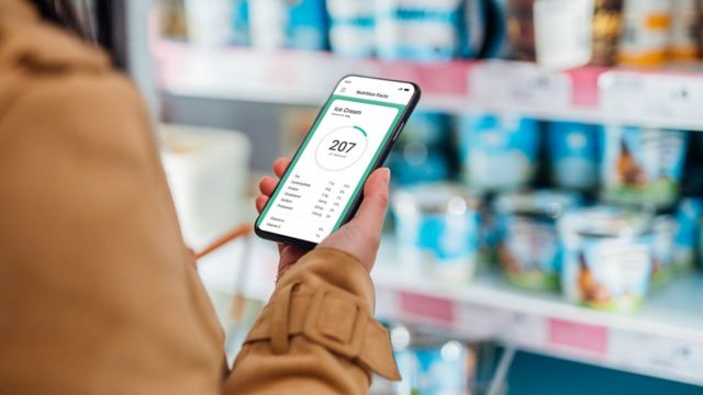 Una mujer revisa en su celular una aplicación que contiene las calorías de cada alimento mientras realiza la compra.