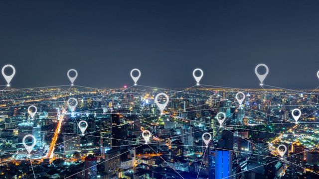 Cidade com vários prédios iluminados durante a noite e símbolos de localização ilustrados e sobrepostos