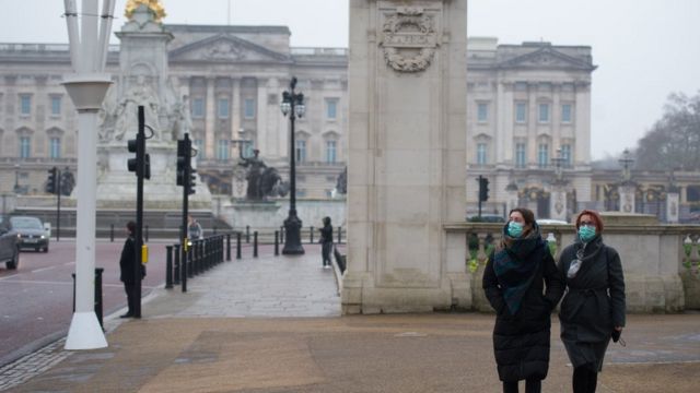 Two people outside Buckingham Palace wear a mask