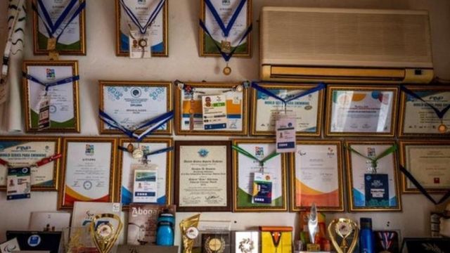 تصویری از مدال‌ها و جوایز الحسین روی دیوار خانه‌اش در آتن