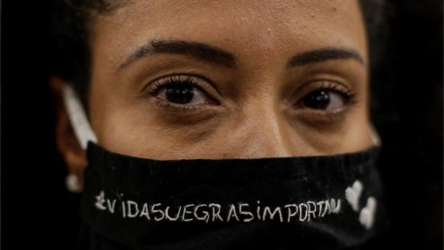 Mulher com máscara em que se lê vidas negras importam