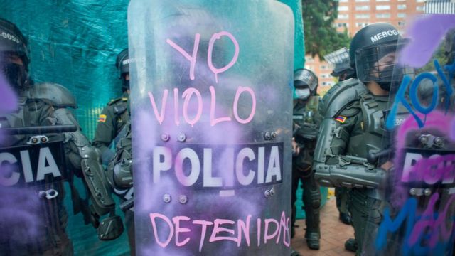 Un policía sostiene un escudo en le que manifestantes escribieron ""yo violo detenidas".