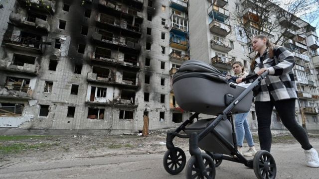 امرأة تدفع عربة أطفال أمام مبنى سكني تضرر بشدة في مدينة تشيرنيغيف شمال أوكرانيا في 3 مايو 2022