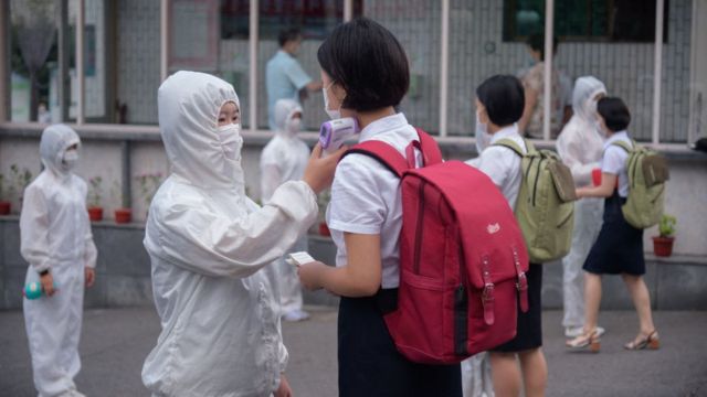 Una funcionaria en traje protector toma la temperatura de una estudiante en Corea del Norte