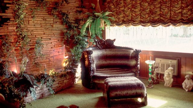 Detalle de la sala de la Selva en la que se ve un sillón enorme en piel marrón con reposapiés, pared de piedra y mucha vegetación.