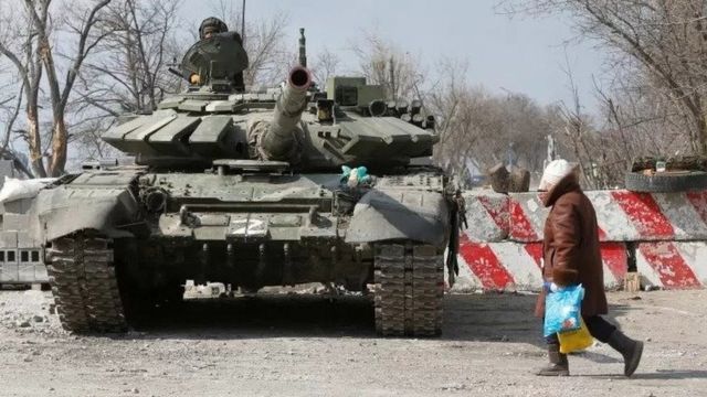 Residents of Mariupol walk past a tank with the symbol Z, which represents support for Russia.