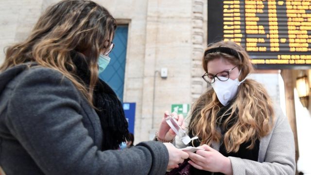 Mulheres de máscara limpam as mãos em estação de trem em Milão, na Itália