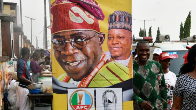 Faixa de campanha eleitoral com foto do ent]ao presidente Buhari ao fundo e em primeiro plano foto do candidato Bola Tinubu