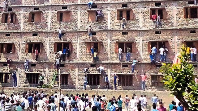 In this photograph taken on March 19, 2015, Indian relatives of students taking school exams climb the walls of the exam building to help pass candidates answers to questions in Vaishali in the eastern state of Bihar
