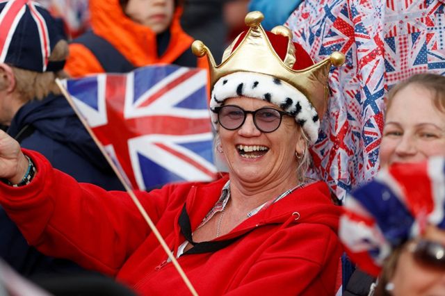 A person waits to watch Britain's King Charles' procession to his coronation ceremony from Buckingham Palace to Westminster Abbey