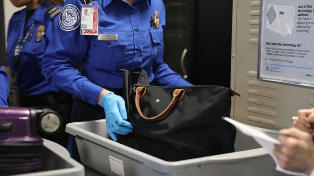 An anonymous TSA official checks a bag in a luggage tray