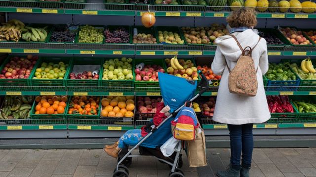 Mulher com bebê escolher frutas em mercado