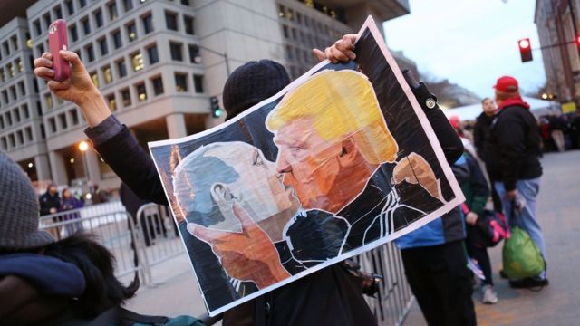Протестующий с плакатом с лицами Трампа и Путина