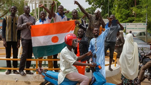 Des hommes brandissent le drapeau du Niger tandis qu'une moto passe devant eux.