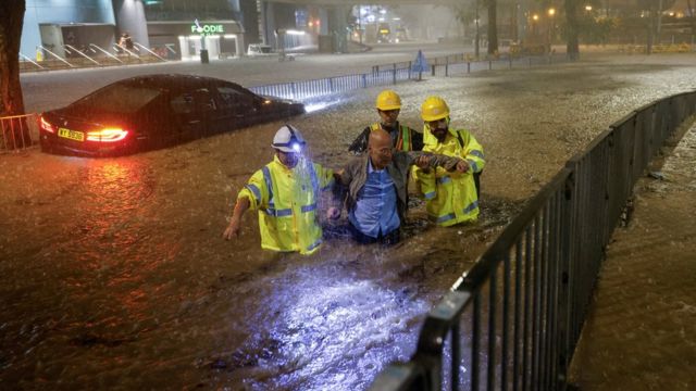 香港某路边疏通沟渠人员搀扶一位被困洪水的司机离开被淹马路（8/9/2023）