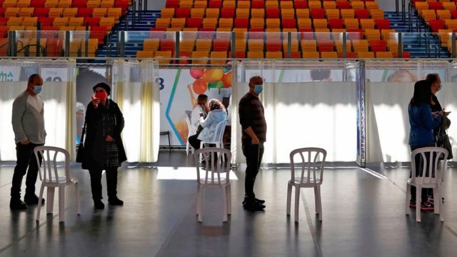 People in Israel waiting to be vaccinated in an impromptu vaccination centre, set up in a sports hall.