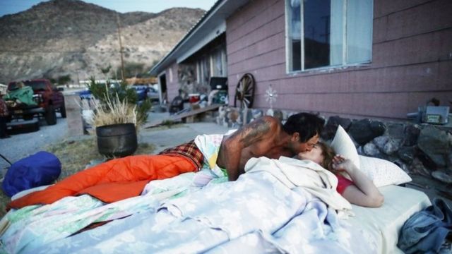 Una pareja se besa mientras está acostada sobre un colchón a las afueras de su casa.