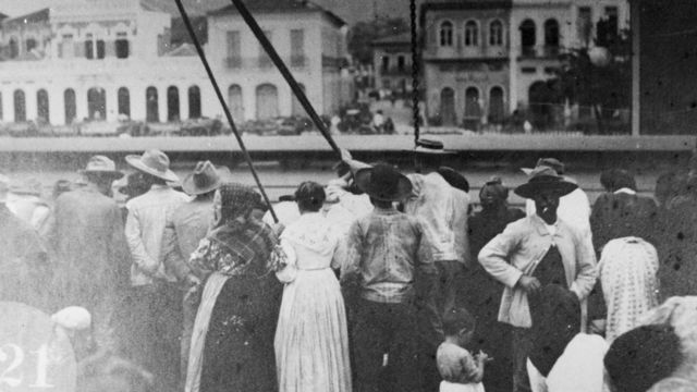 Foto em preto e branco mostra dezenas de homens e mulheres no porto