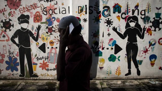 Warga melintas di depan mural bertema menjaga jarak di Kemplayan, Solo, Jawa Tengah, Minggu (21/2/2021).