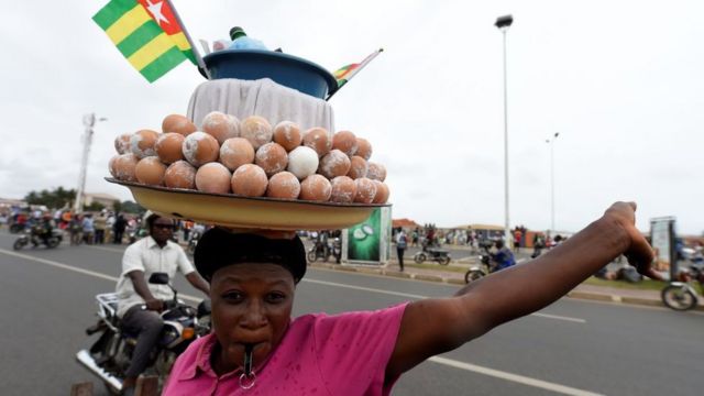 Jeune revendeuse d'œufs bouillis avec un drapelet togolais au-dessus de sa marchandise posée sur sa tête